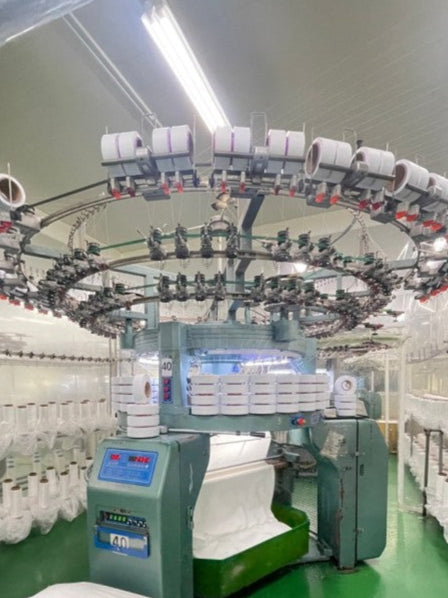 A large, industrial circular knitting machine with numerous spools of white yarn.